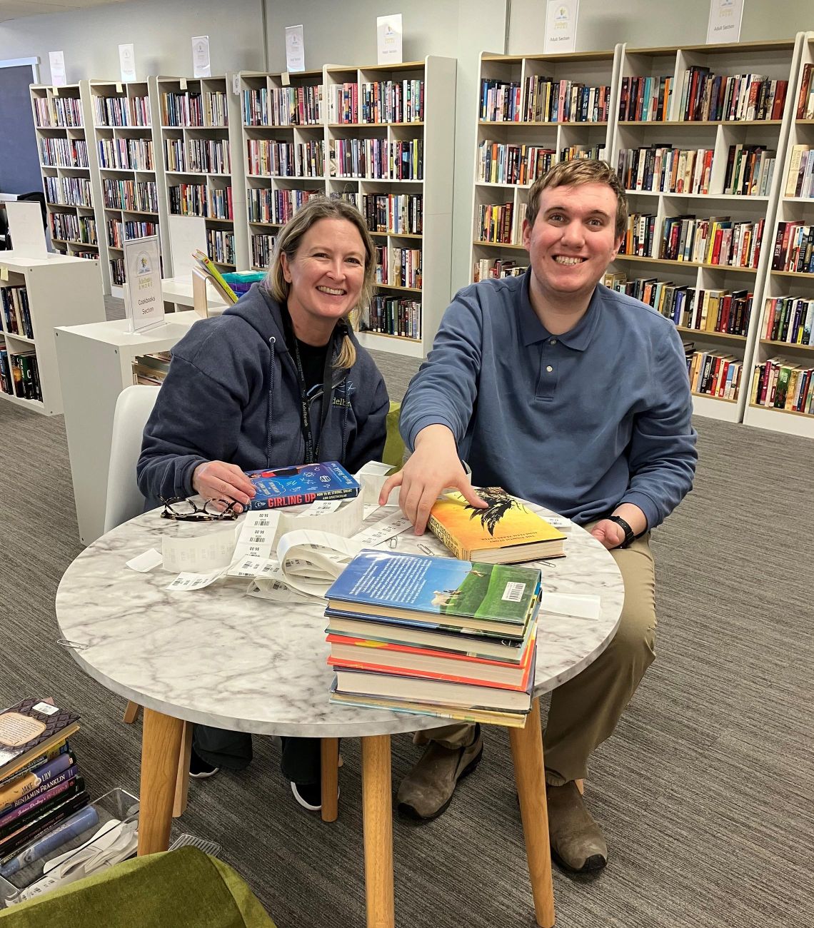 Two people sitting at a table with books, smiling