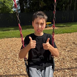Young boy sitting on a swing with two thumbs up