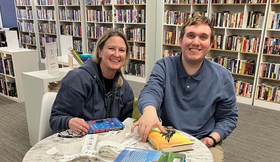 Woman and young man smiling while sitting at a round table with books in front of them