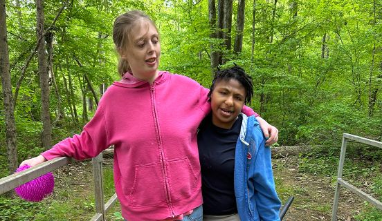 Two young woman walking on a trail in the woods with their arms around each other