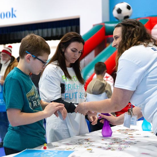 A woman giving another woman and little boy a handout at a table