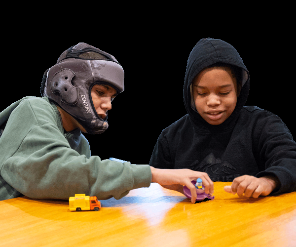 Two boys sitting next to each other and playing with toy cars