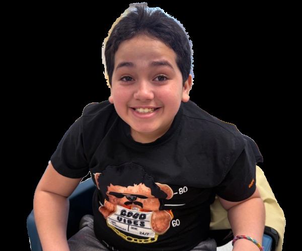 Boy in a black t-shirt, sits in a blue chair, smiling for the camera