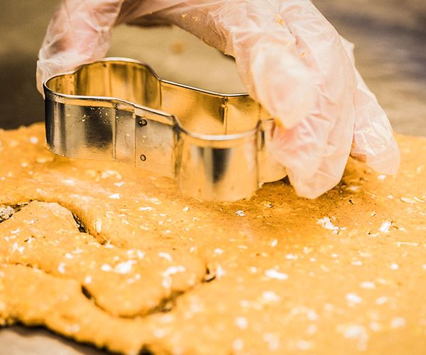 A gloved hand holds a bone shaped mould, pressing imprints into the dough.