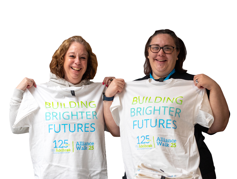 Two women smiling while holding up the Alliance Walk 25 t-shirts that say "Building Brighter Futures"