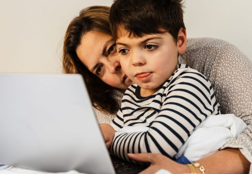 A child and their guardian looks at a laptop screen.