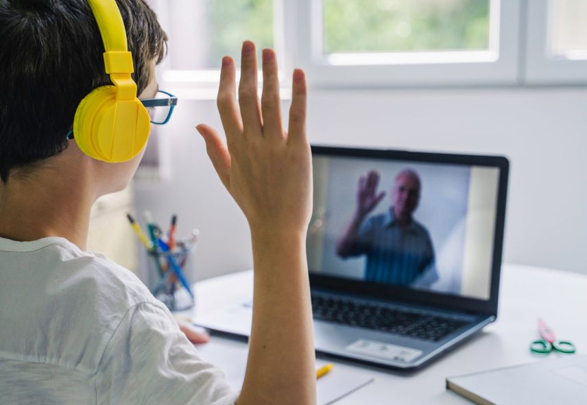 A young boy waves to his teacher through a computer screen