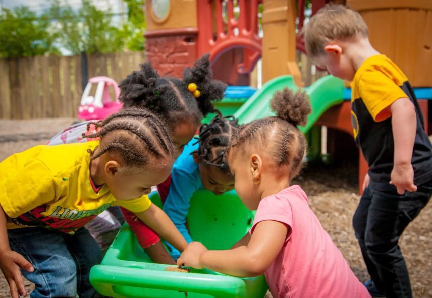 Kids digging in a large green bucket in a playground