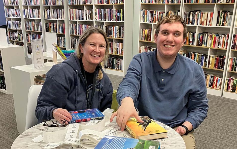 Woman and young man smiling while sitting at a round table with books in front of them