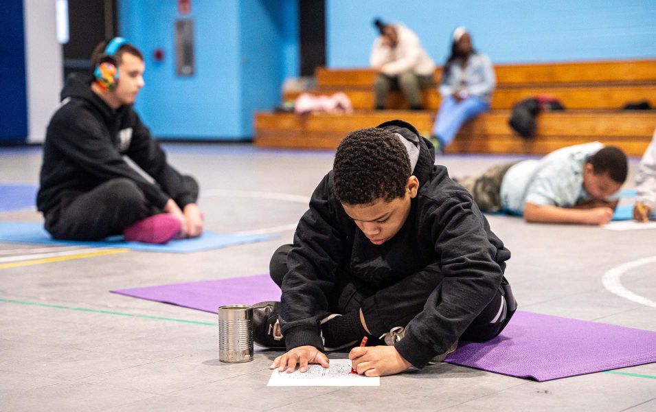Young boy sitting on a yoga mat and coloring in a picture with a red crayon