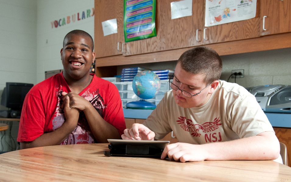 Two young men sitting next to each other while one is using an iPad