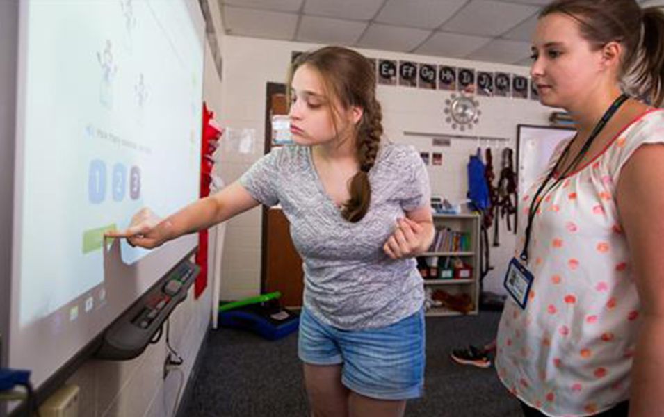 Girl using a SmartBoard with adult supervision
