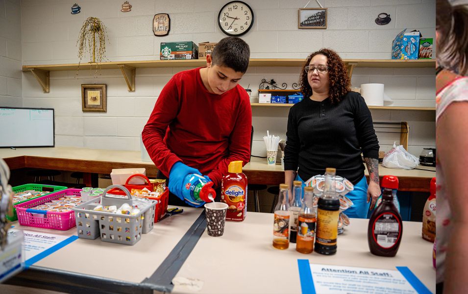 Boy pouring creamer into coffee while a woman supervises him