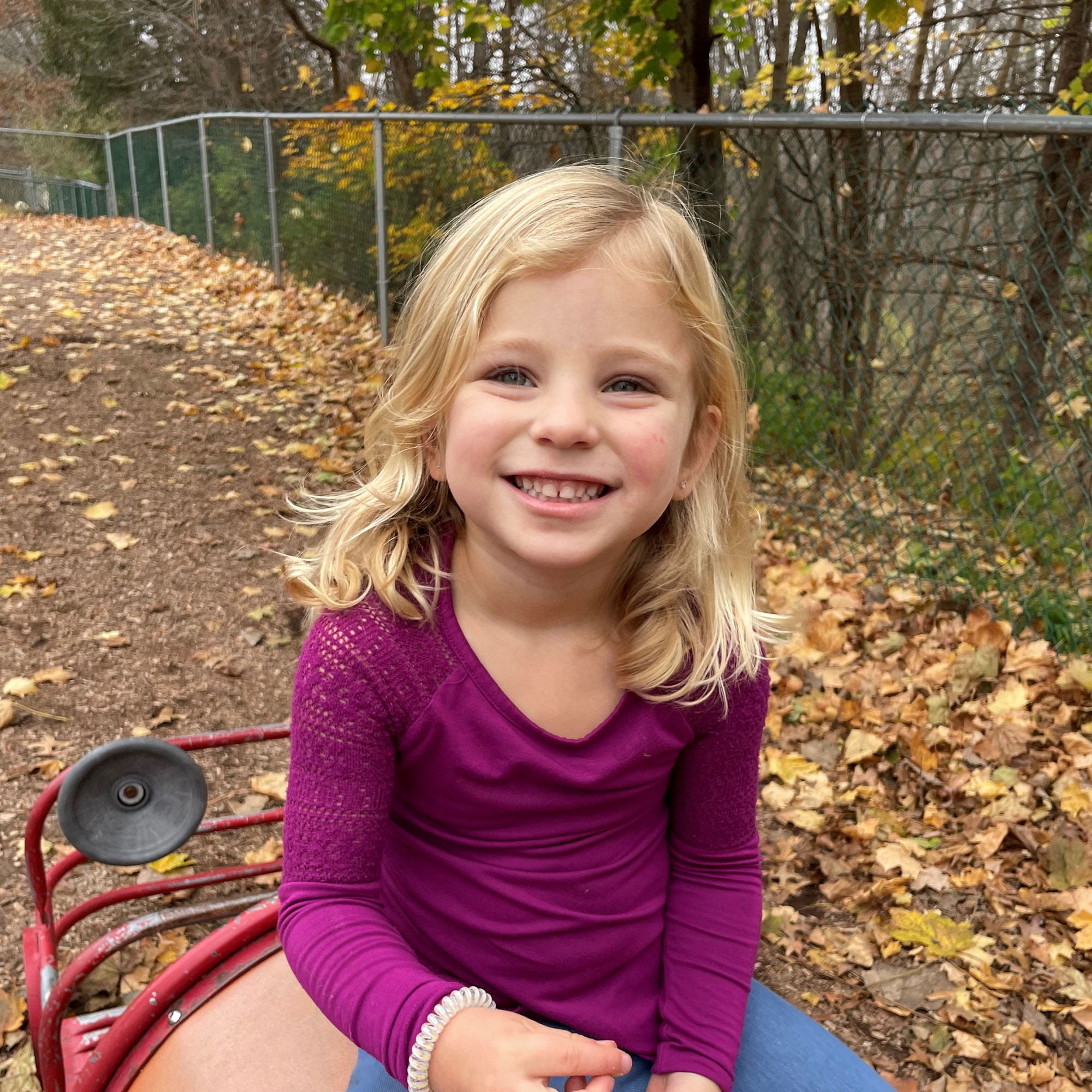 A young girl sits at the playground and smiles for the camera.